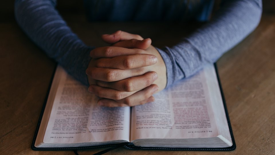 hands folded in prayer on top of Bible