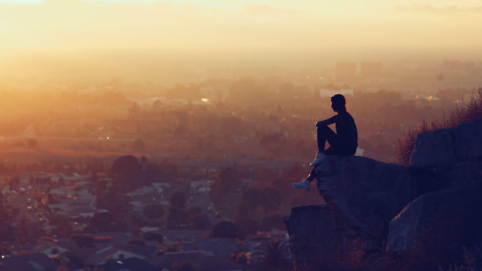 kid sitting on a rock above a city