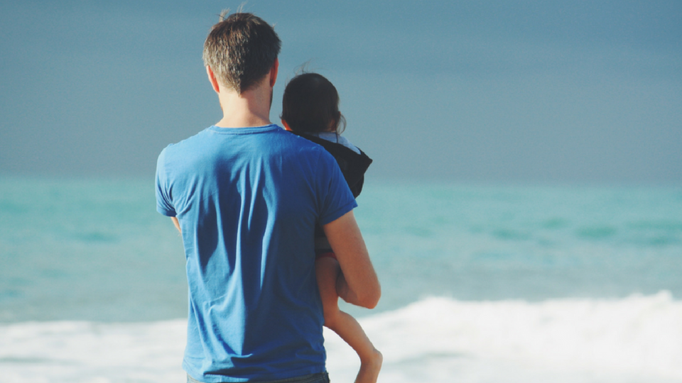 man holding daughter looking out at ocean