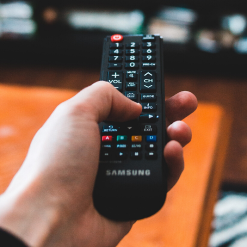 person holding black remote pointing it towards a large flat screen tv
