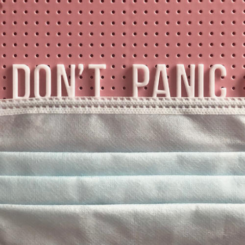 words "don't panic" spelled out on a letter board with a medical mask lining the bottom of them