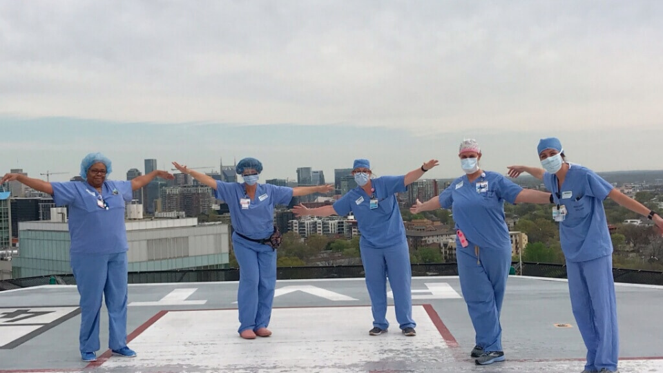 five nurses standing on a helicopter pad of a hospital with their arms stretched out beside them