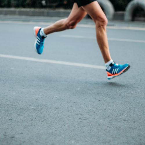 person's legs running on a black pavement road with blue tennis shoes on