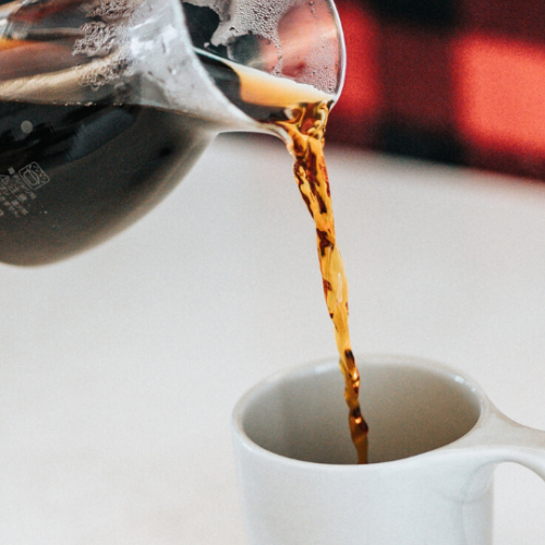 closeup of coffee from a coffee pot being poured into a white coffee mug