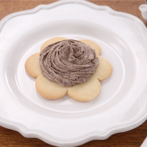 white plate with a flower-shaped sugar cookie on it and grey icing on top of cookie