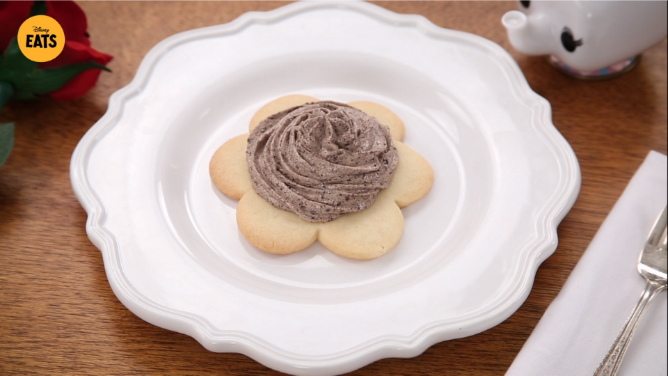 white plate with a flower-shaped sugar cookie on it and grey icing on top of cookie