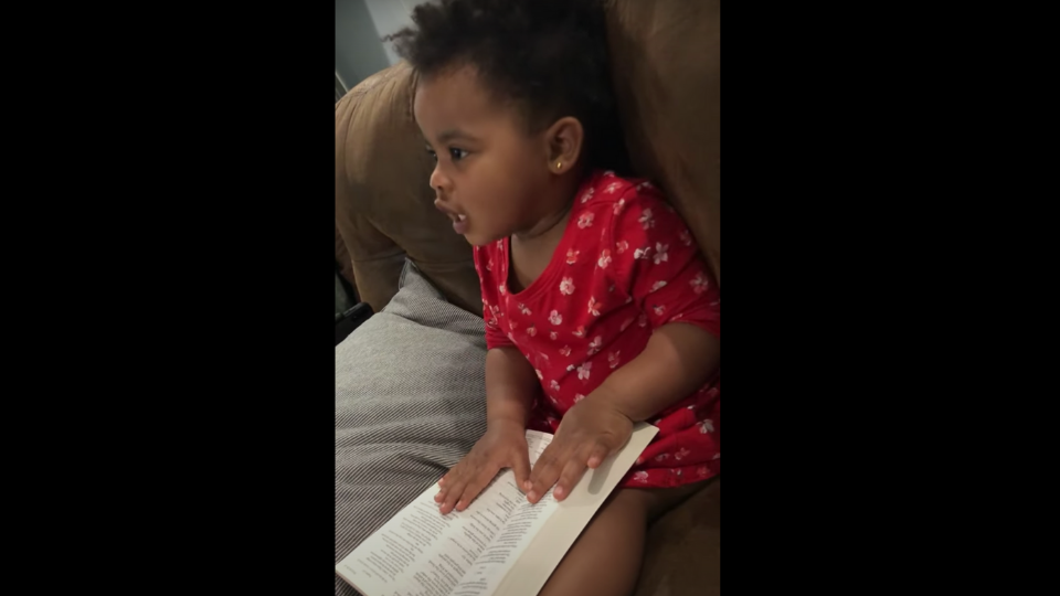 Little girl sits on couch holding a Bible in her lap