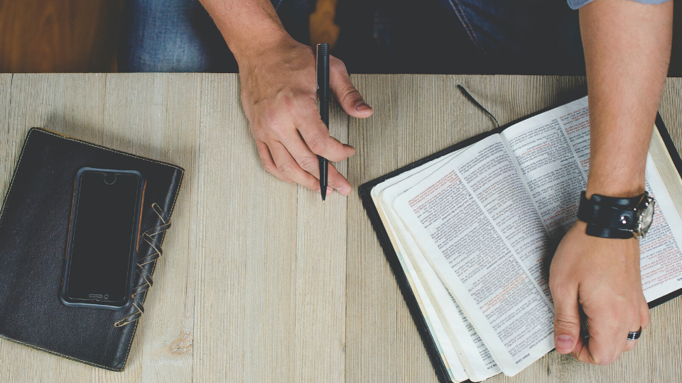 overhead shot of a person with a Bible and a notebook holding a pen