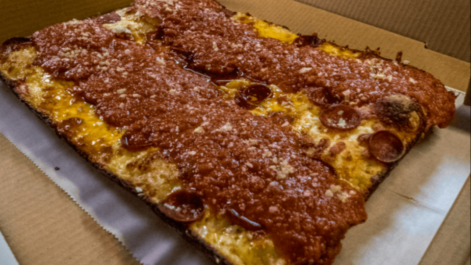 Detroit style pizza with sauce on top and cheese on the bottom sitting in a brown pizza box