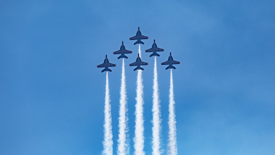six navy air planes forming a triangle as they shoot upwards towards a blue sky