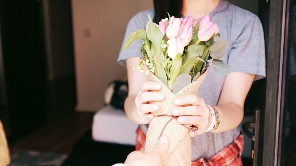 woman in a light grey shirt reaching out to hold pink tulips