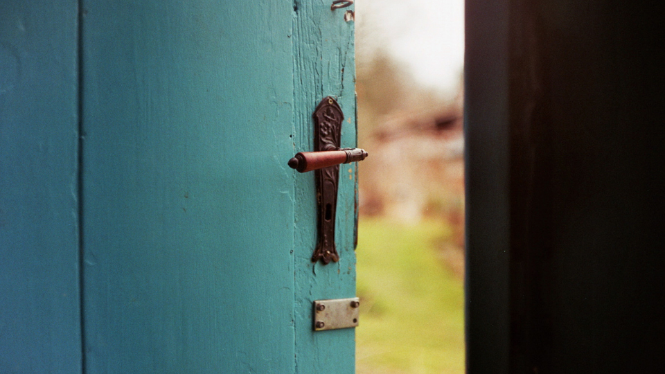 turquoise wooden door cracked open leading outside to a yard of green grass