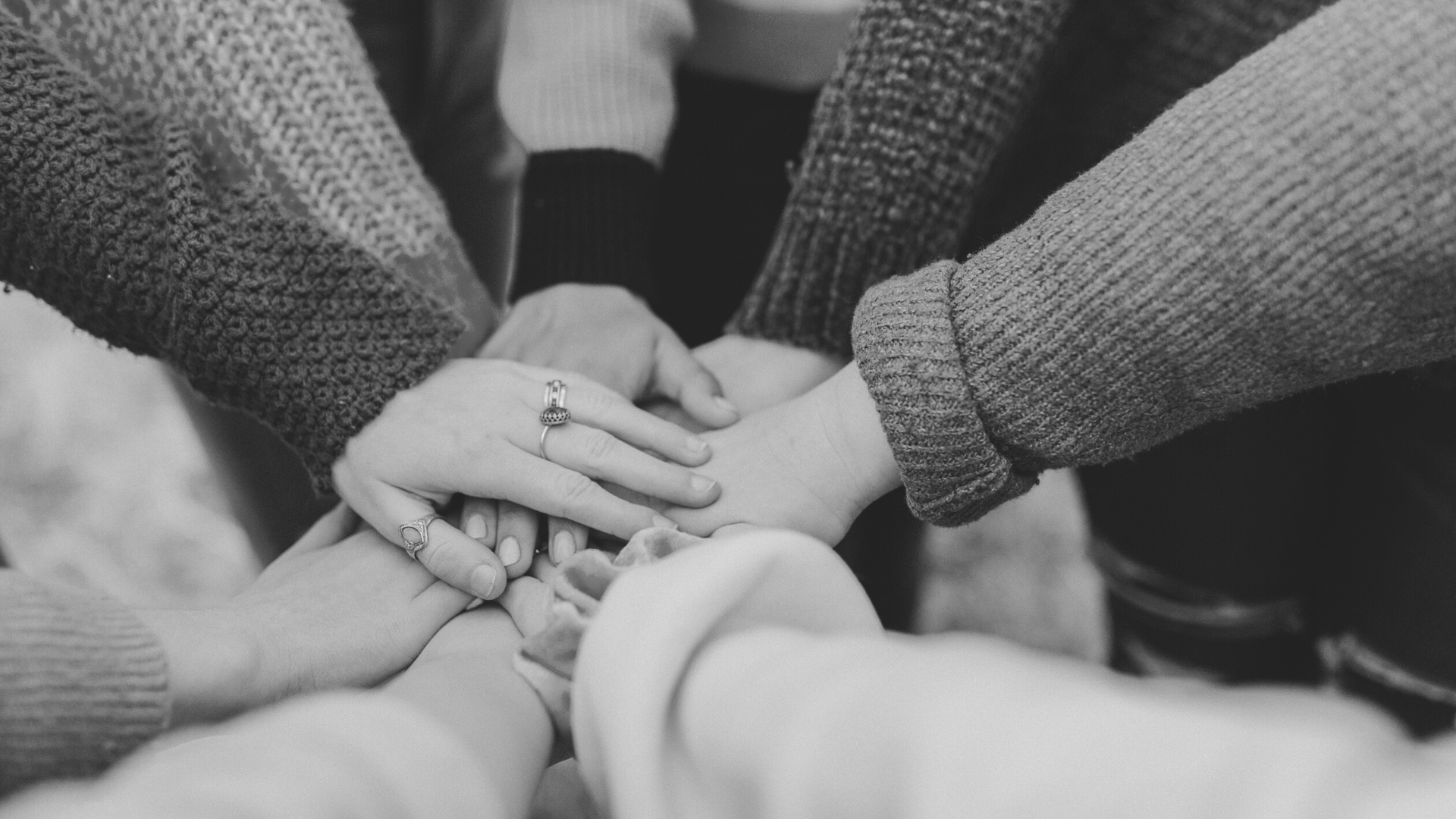 black and white photo of people gathering in a circle and stacking their hands together