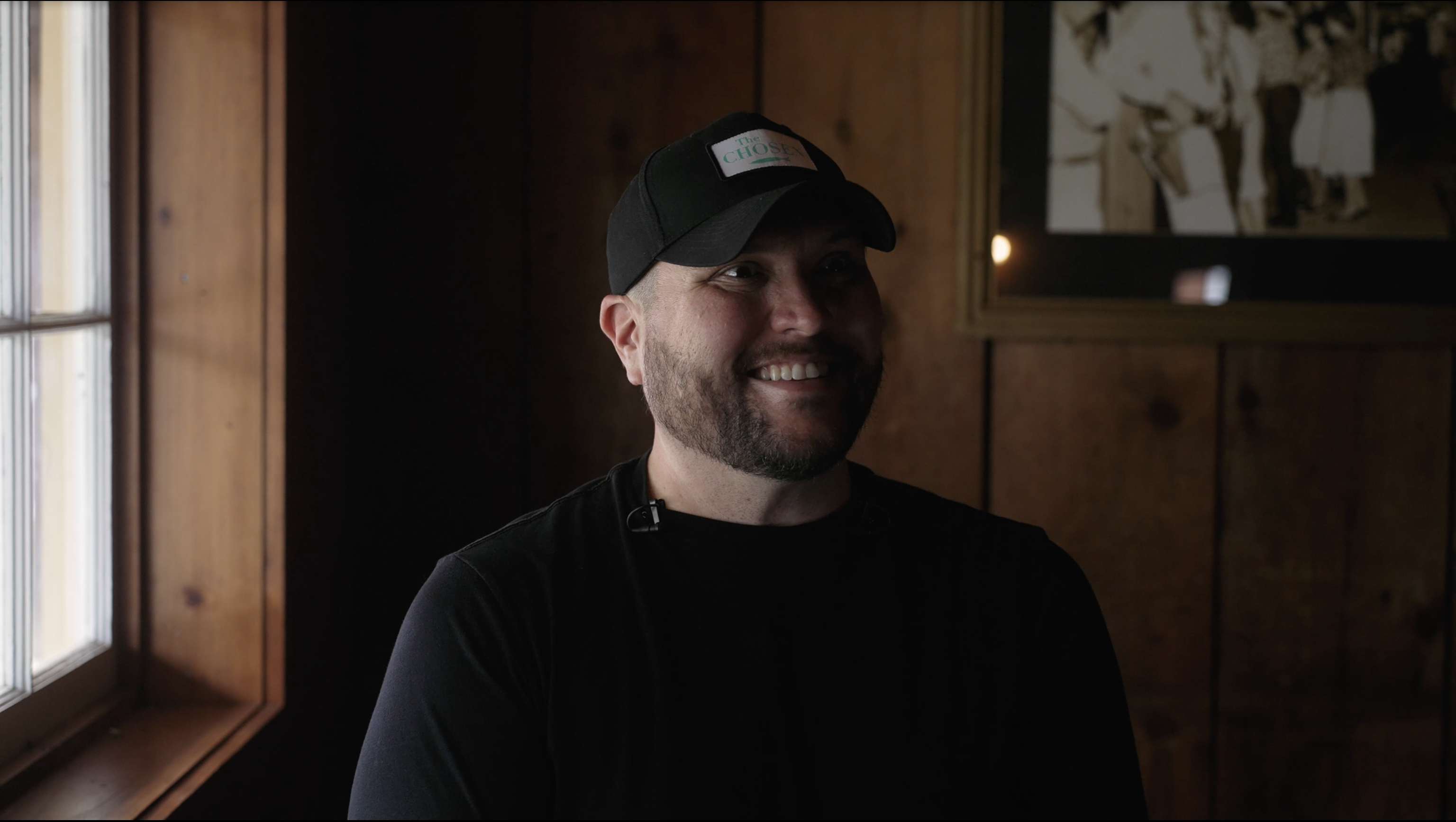 Micah Tyler wearing a black shirt and black baseball cap as he smiles at the camera during his most recent BRIGHT-FM interview