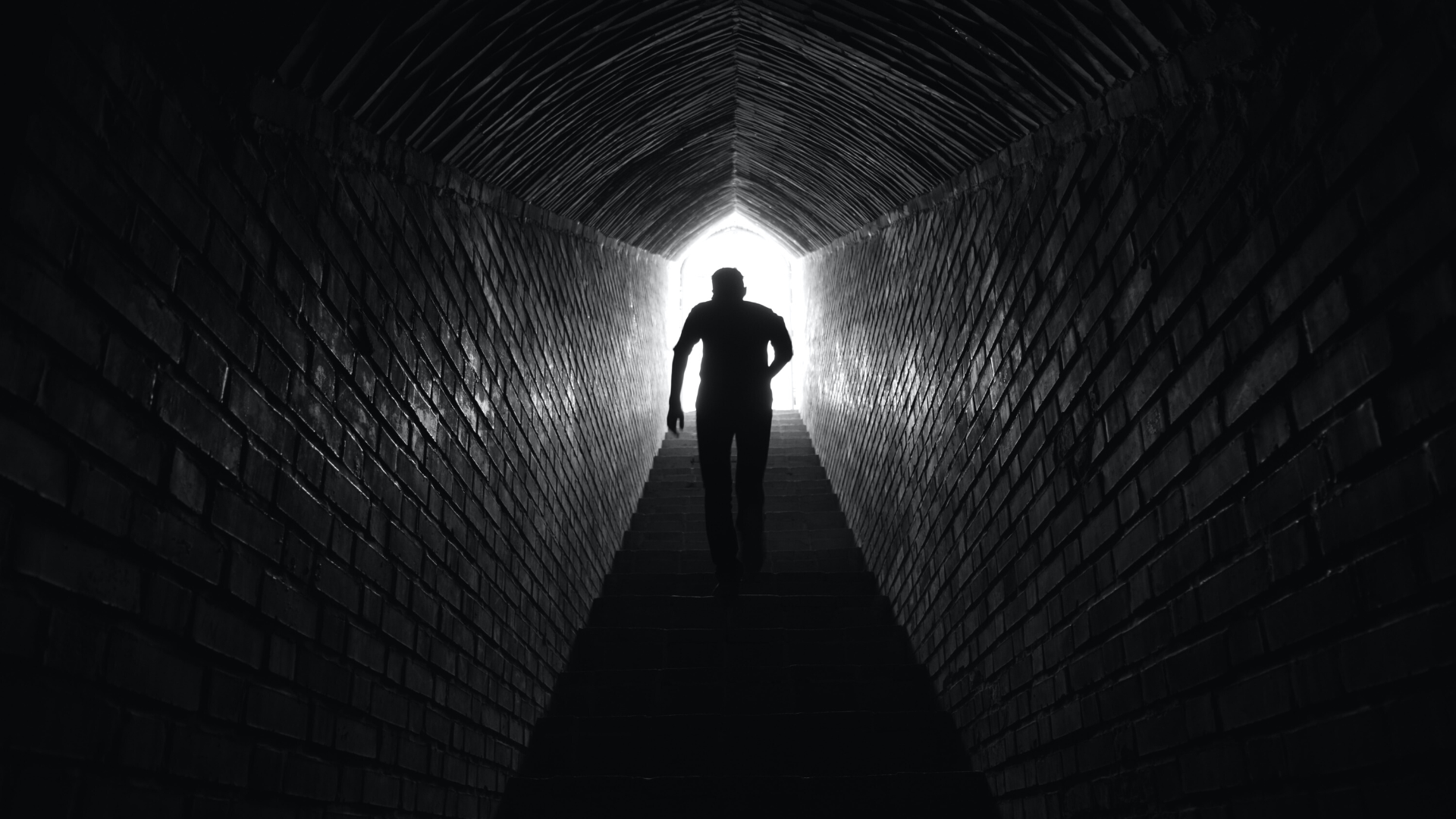 person walking up stairs in a dark tunnel as light shines through from the top