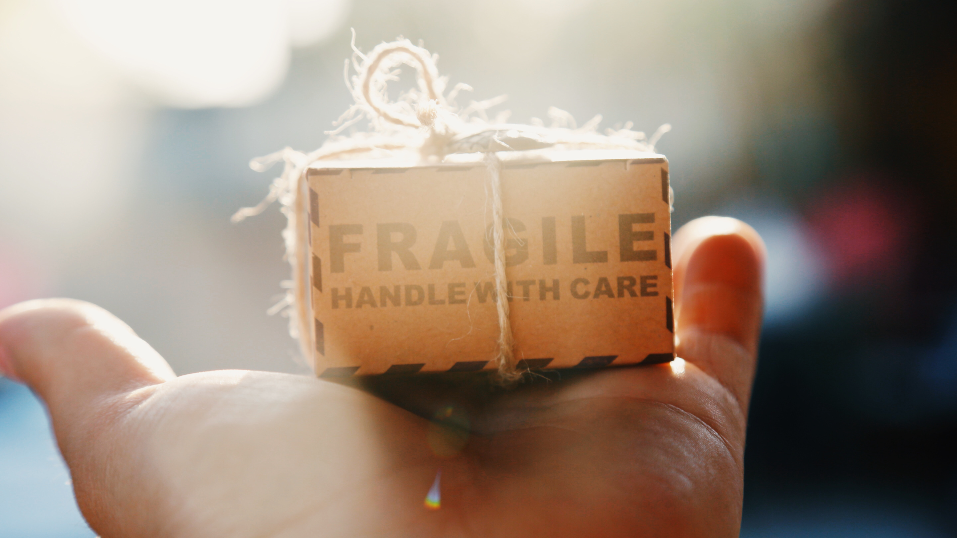an outstretched palm holding a small cardboard box that reads FRAGILE HANDLE WITH CARE