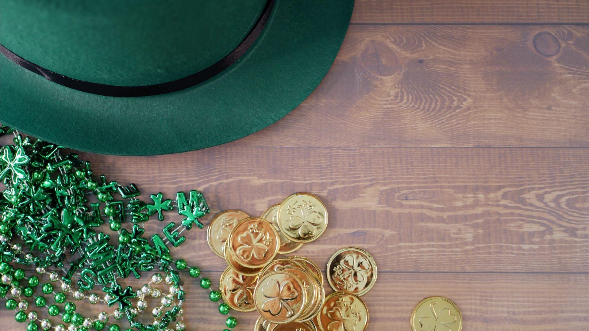 green hat, gold coins, and a green Irish necklace all sitting on a wooden table