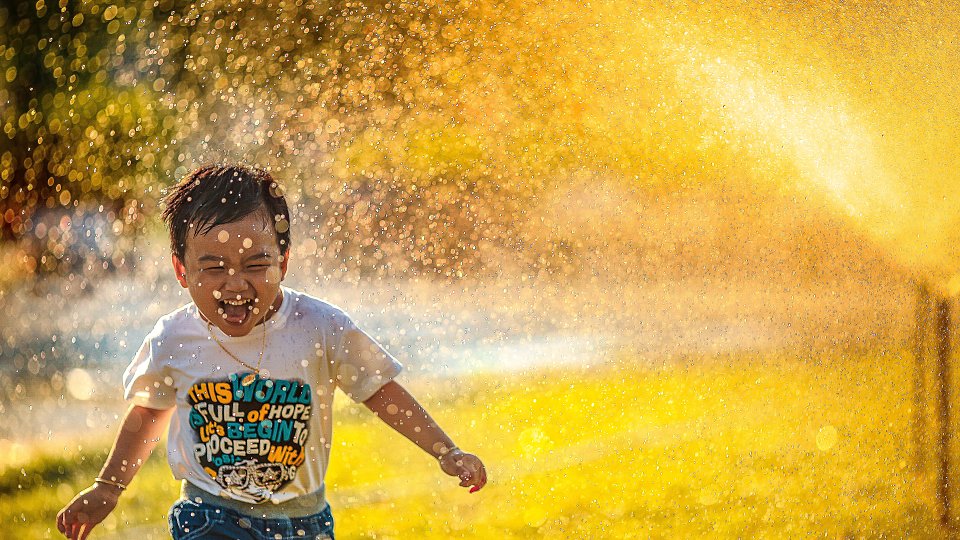 Little boy laughing and running through sprinkler