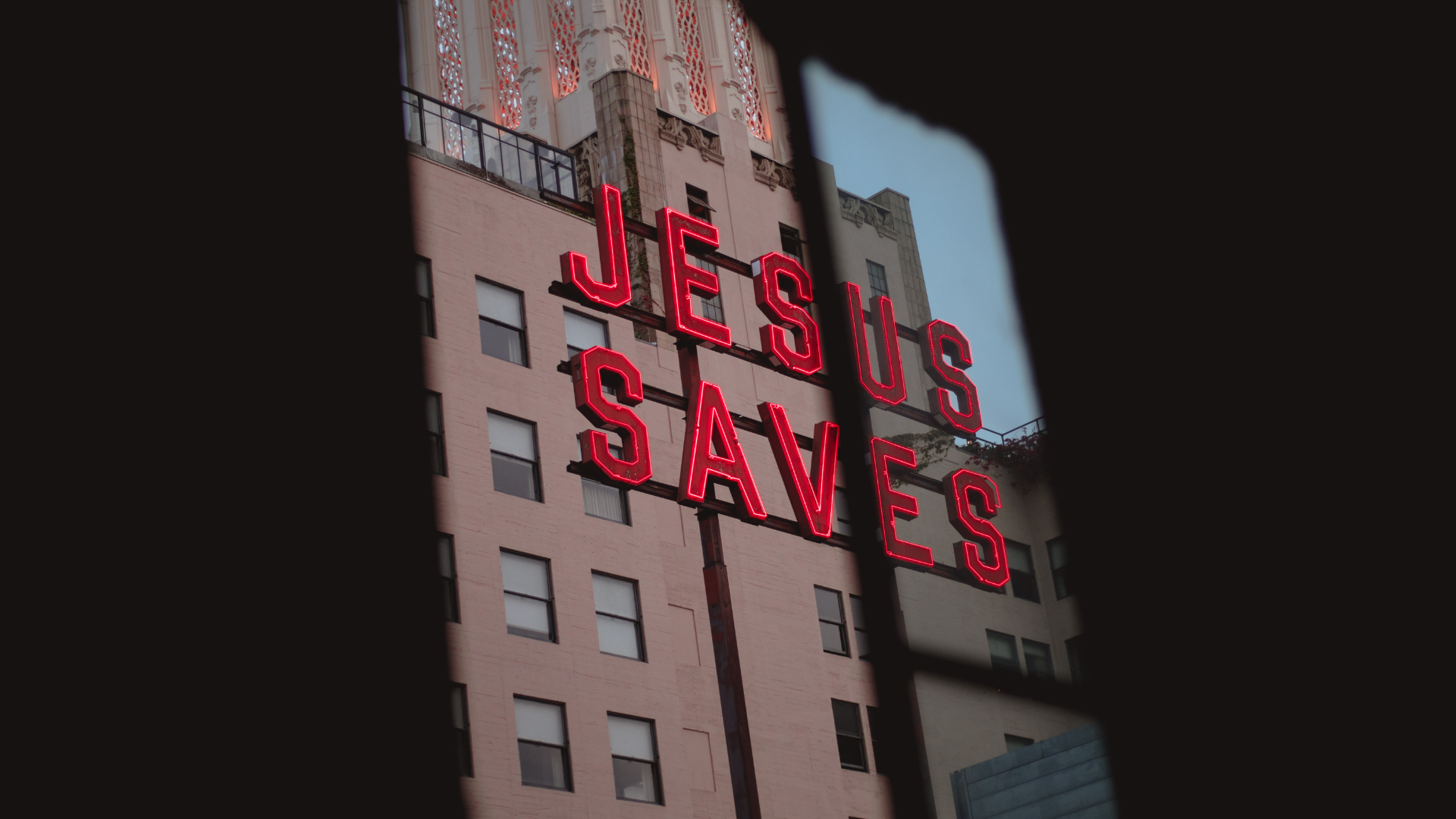 view looking out a window to a Jesus Saves neon sign on a city building