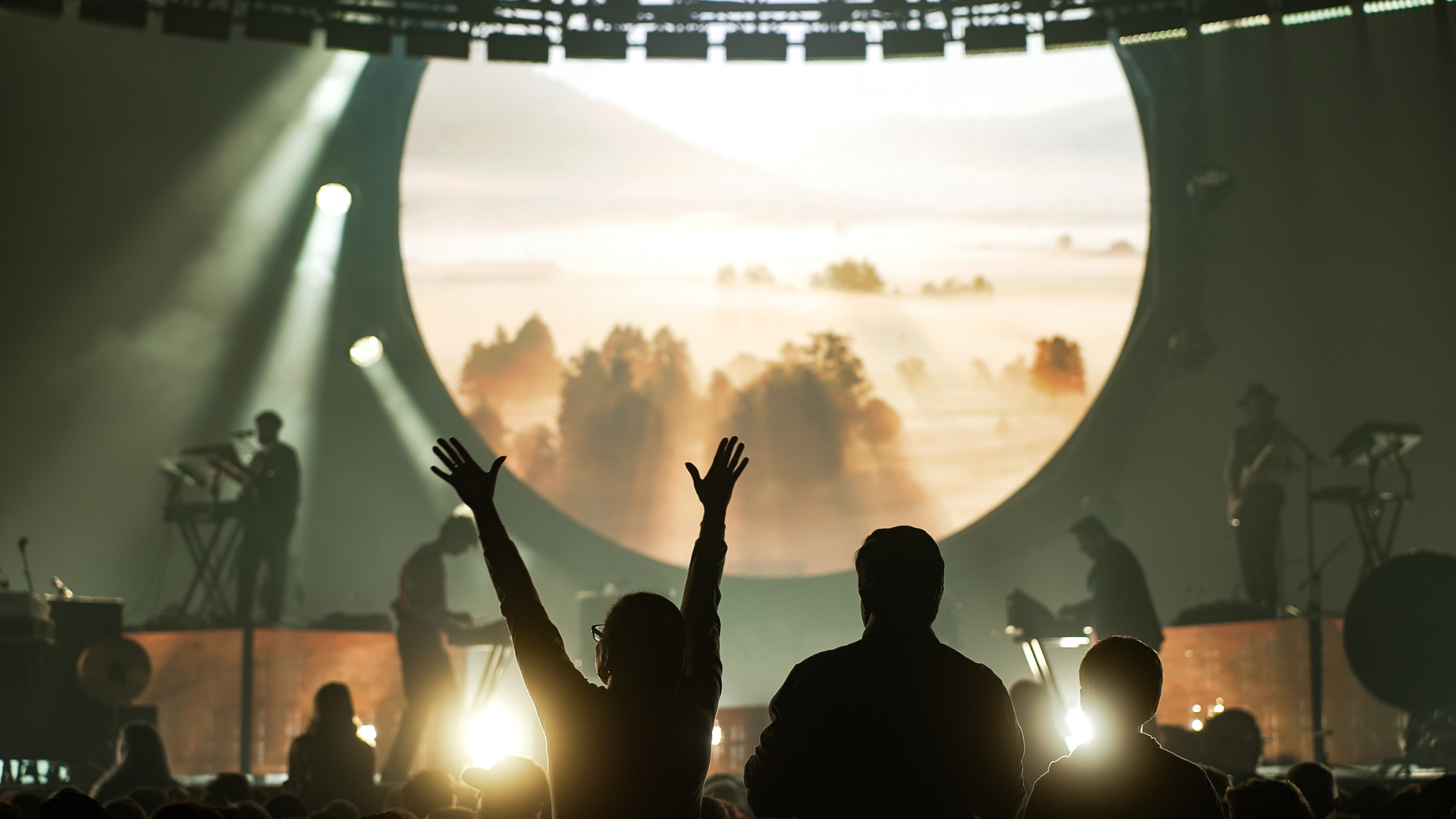 A woman and man standing side by side with their hands raised while worshiping at a for KING & COUNTRY concert