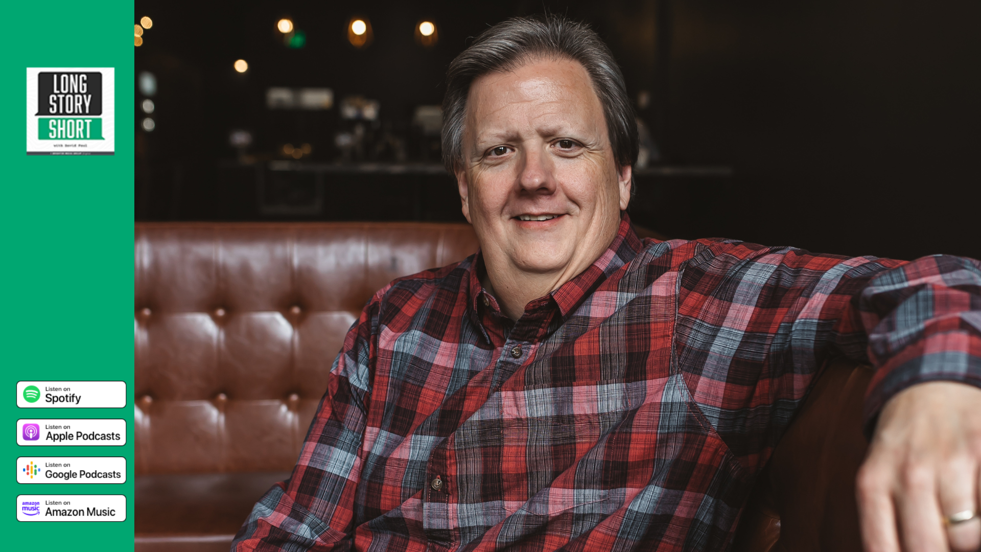 Mike Alley wearing a red and grey plaid shirt while smiling and sitting on a brown leather couch