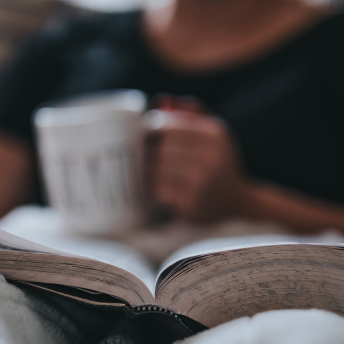 Person sitting in a chair reading the Bible while holding a mug and snuggling in a blanket