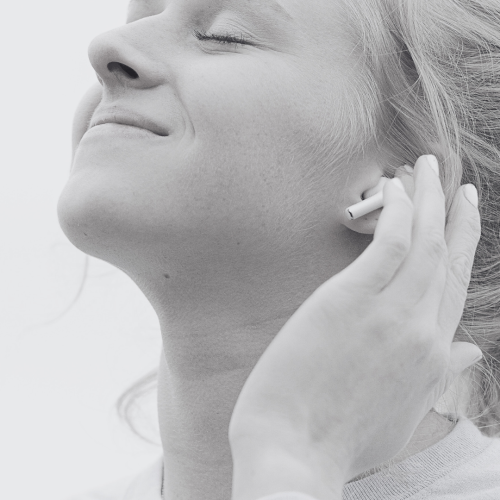 Woman listening to music on airpods and smiling up at the sky